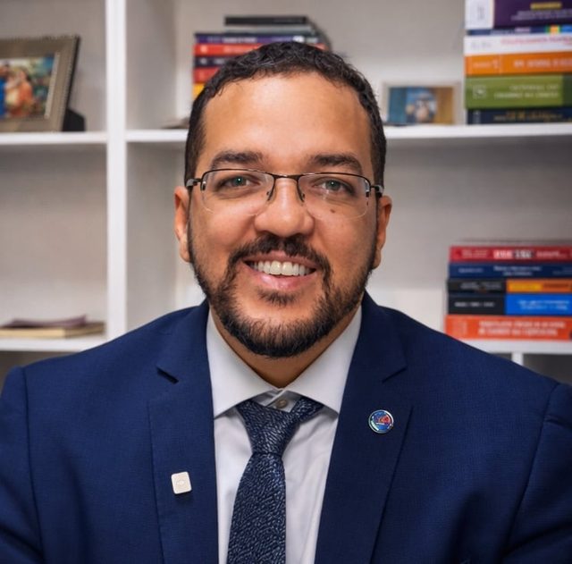Carlos Eduardo Silva, advogado, de terno azul, diante de estante de livros